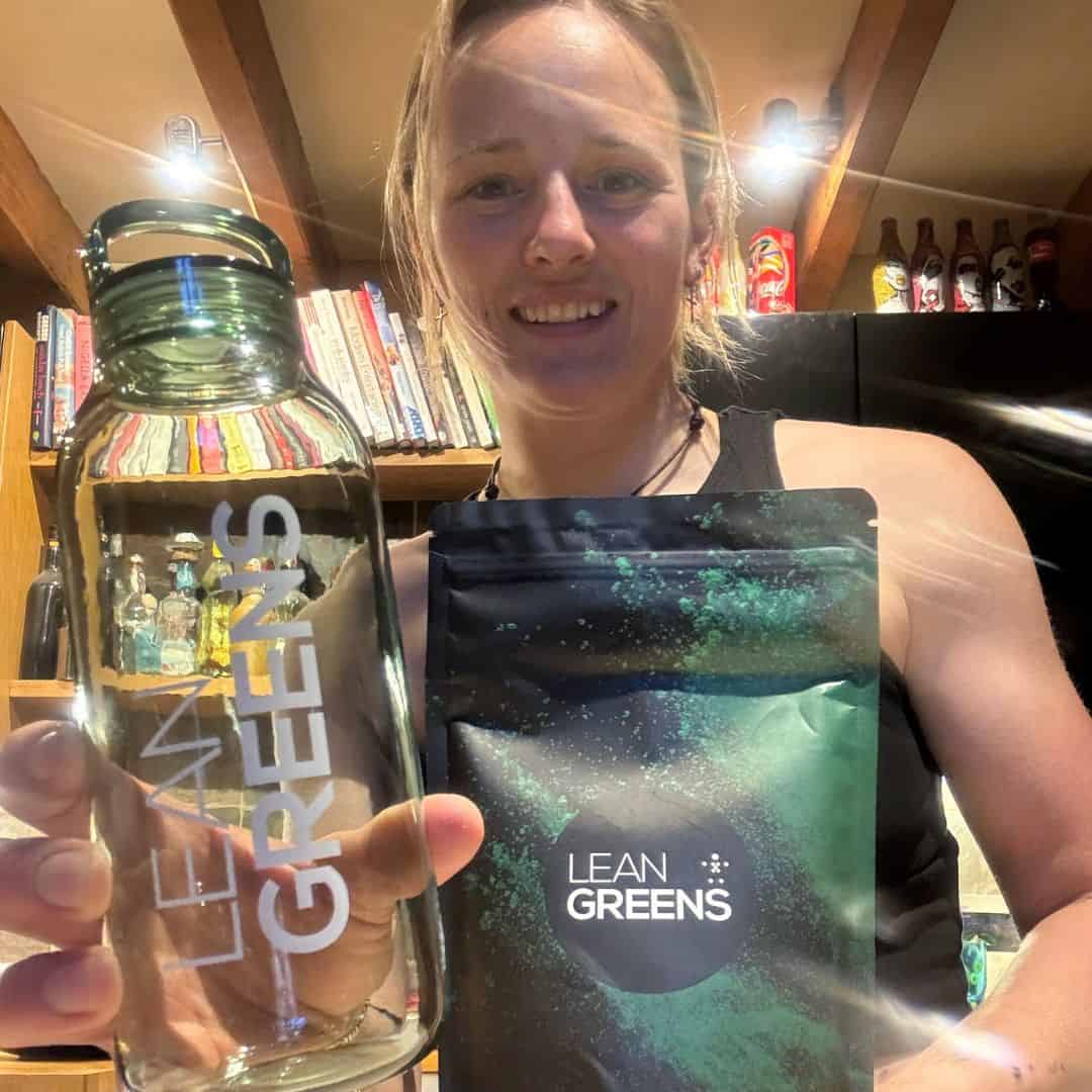 Woman holding a pack of Lean Greens and a clear water bottle, ready to mix a super greens powder from the UK
