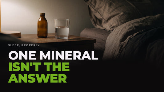 A dark bedside table at night with a glass of water and a small amber bottle beside a rumpled duvet, captioned “One mineral isn't the answer”.