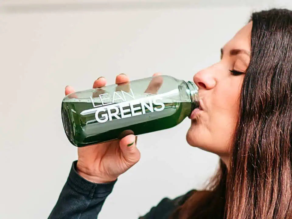 Person drinking collagen greens from a 'Lean Greens' bottle against a plain background