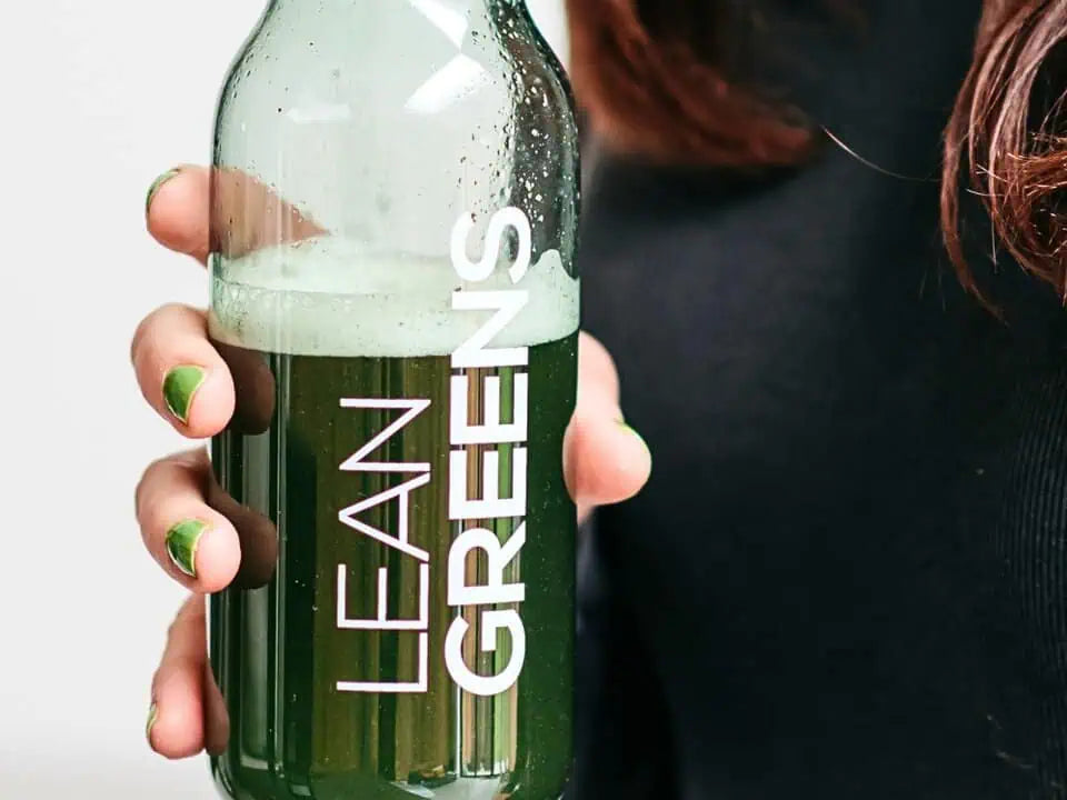 Person holding a bottle containing collagen greens labeled 'Lean Greens' with a white background