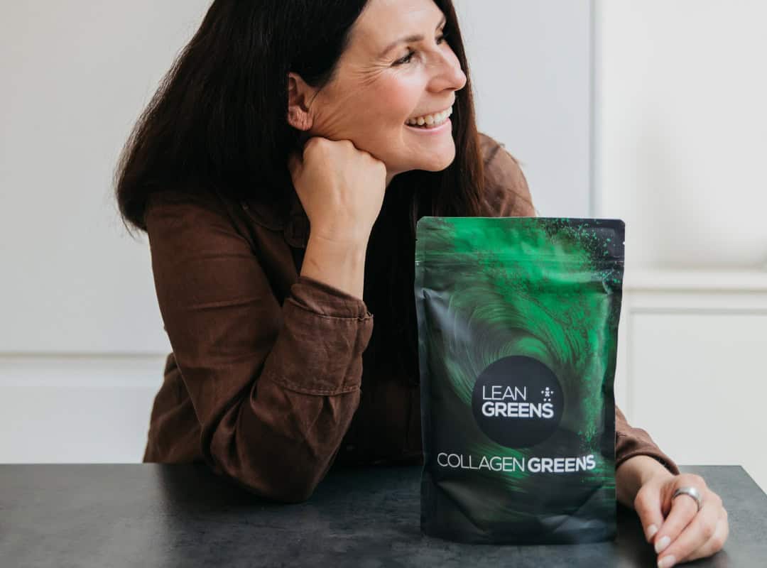 Woman sitting at a table with a bag of Lean Greens Collagen Greens - UK alternative to AG1