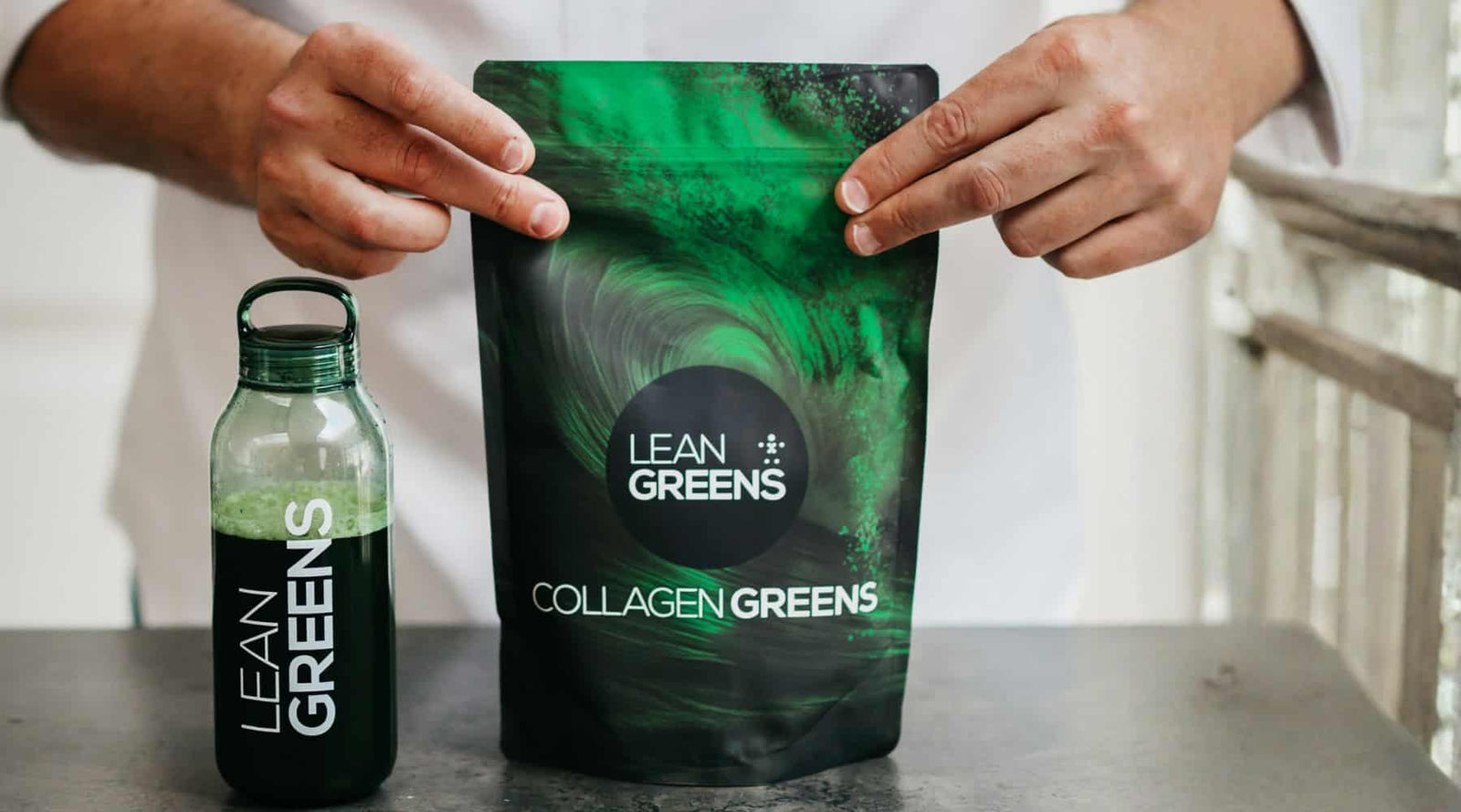 Person holding a package and bottle of Lean Greens Collagen Greens on a table.