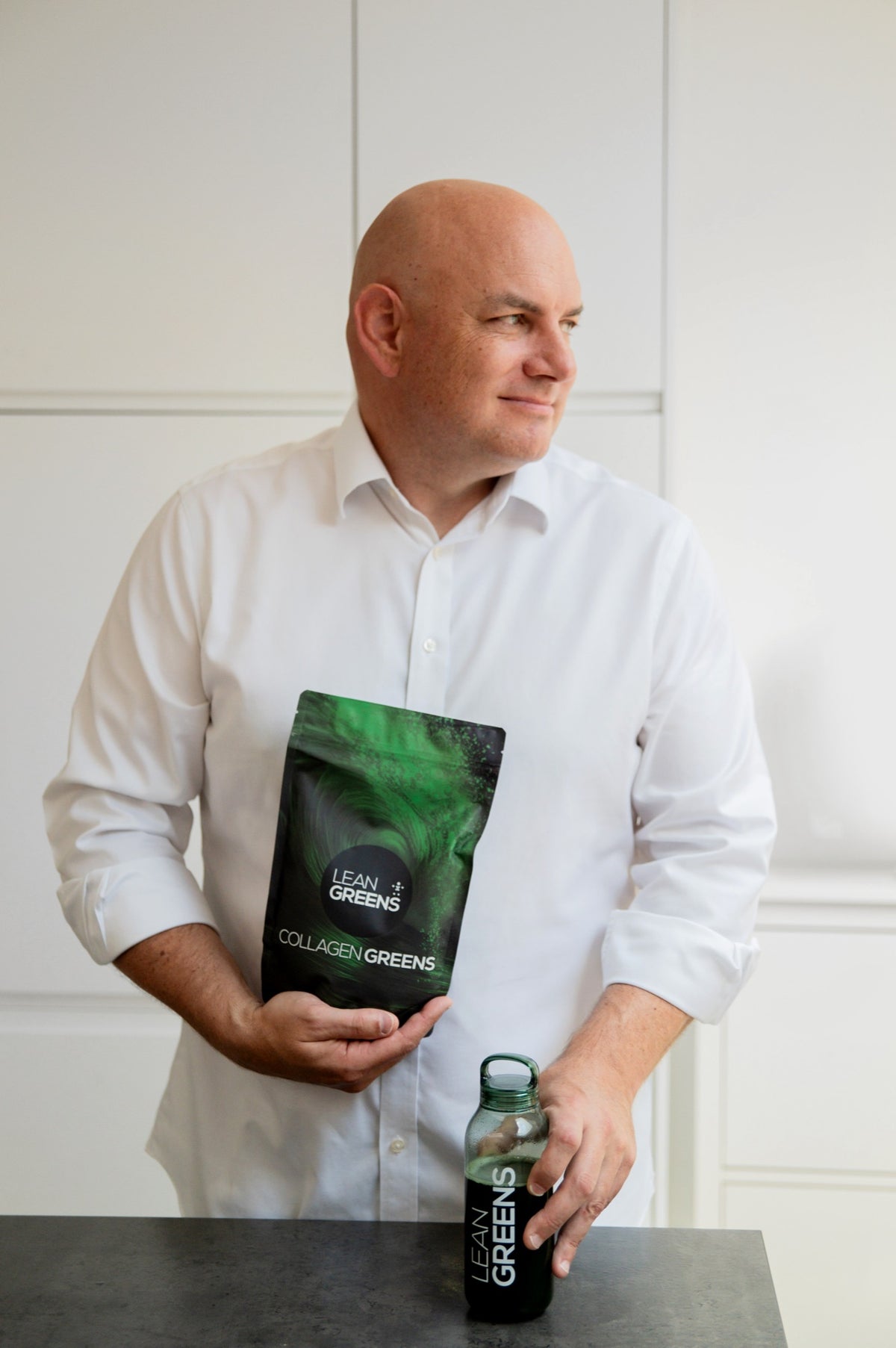 Tim, co-founder of Lean Greens, in a white kitchen holding a pouch of Collagen Greens