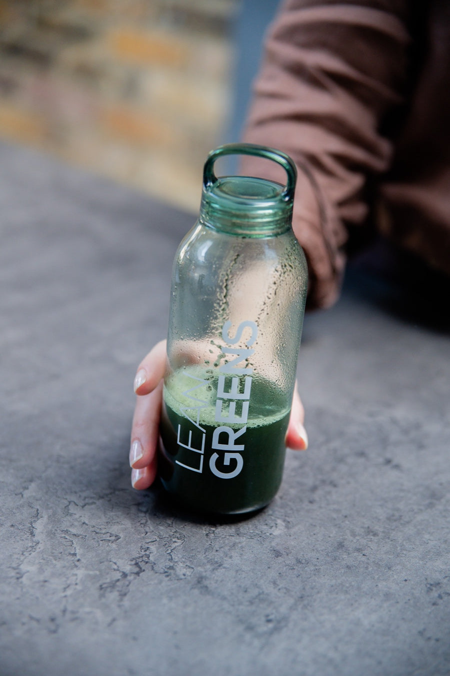 A hand holding a shaken bottle of Collagen Greens, mixed and ready to drink