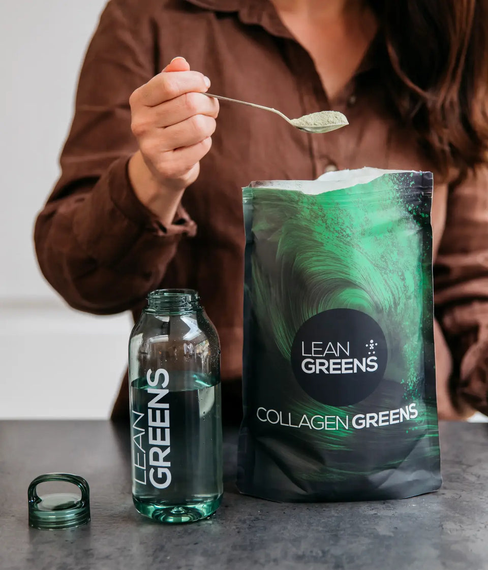 A spoonful of Collagen Greens powder lifted from an open pouch, beside an empty water bottle
